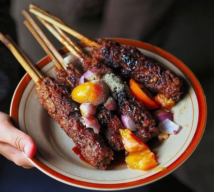 Sate Buntel berwarna kecokelatan dari kecap dan daging yang dibakar dan juga potongan tomat segar beserta taburan lada putih