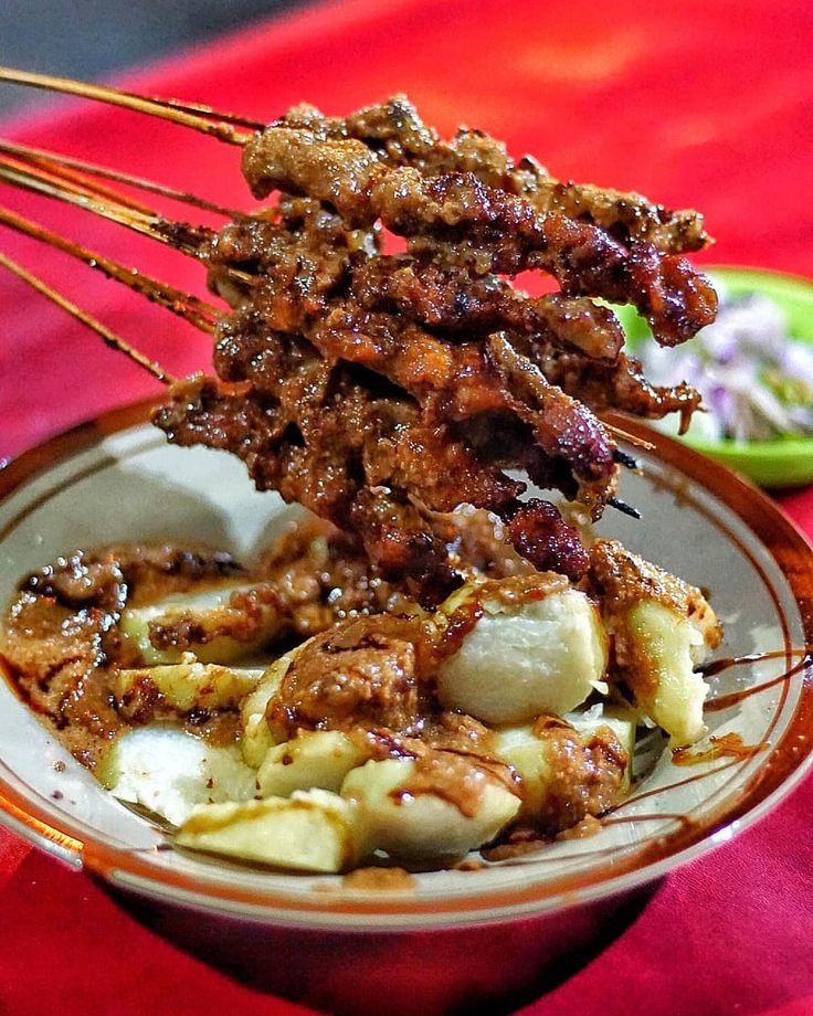 Sate madura dengan lontong di atas piring yang dilumuri dengan saus bumbu kacang dan kecap